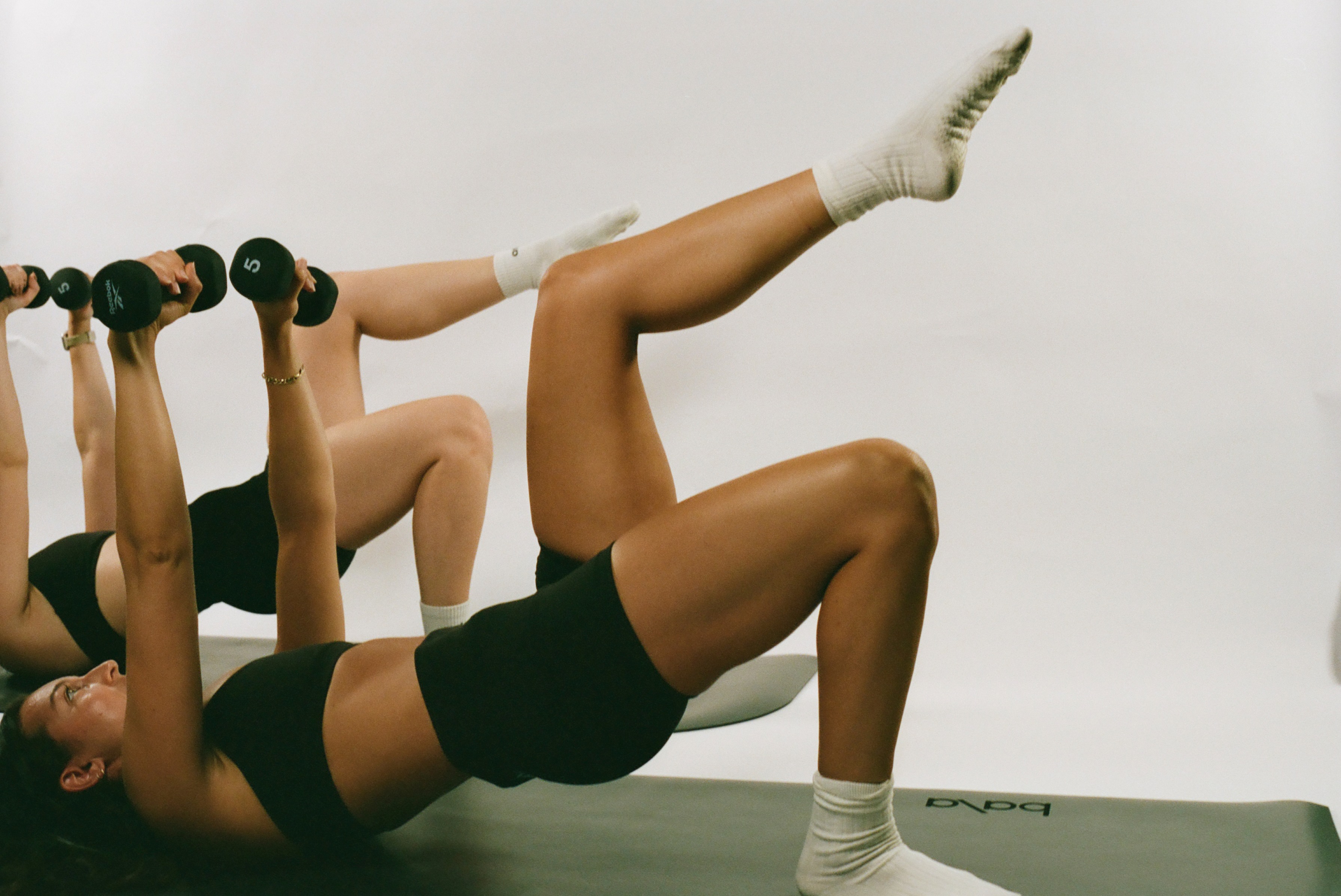 Members pressing dumbbells overhead on mats during a Strength class at Powered