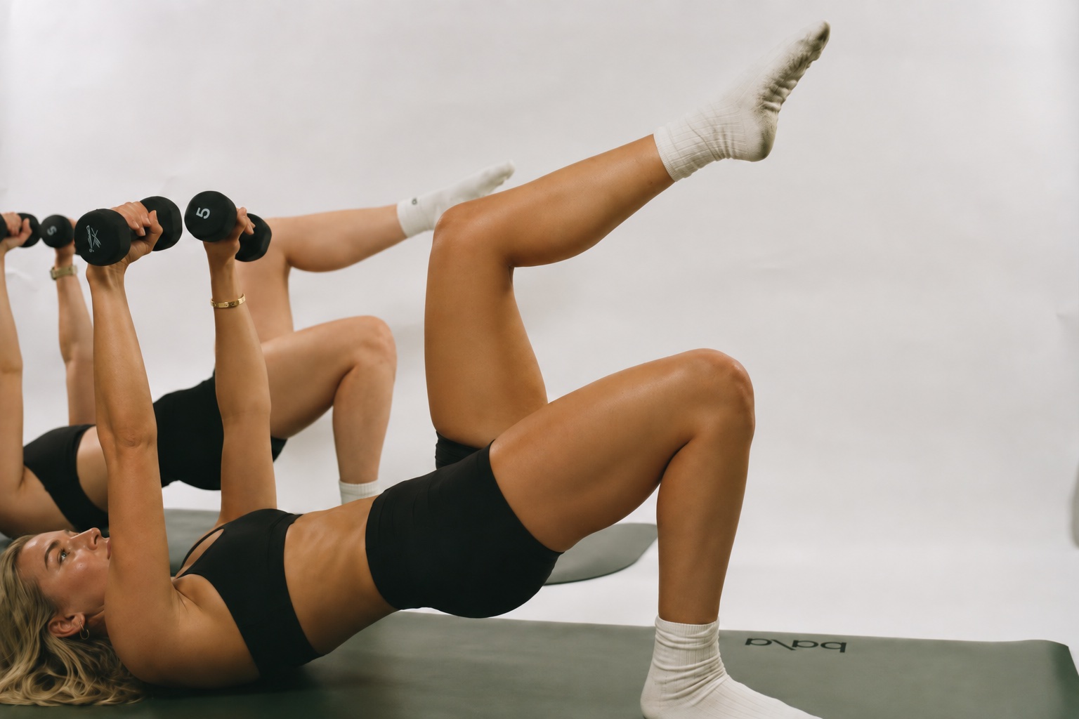 Members doing a dumbbell chest press from a single-leg glute bridge during a Strength class at Powered